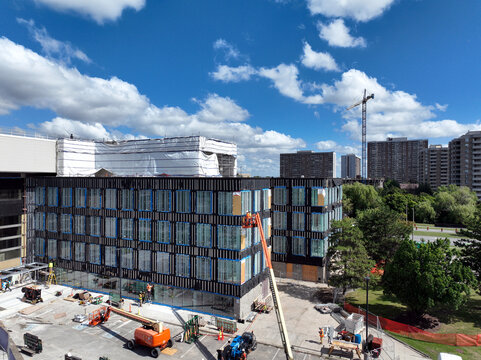 Aerial view of a contemporary multi-storey building under active renovation construction, featuring a black steel and glass wall facade with workers and equipment on site.