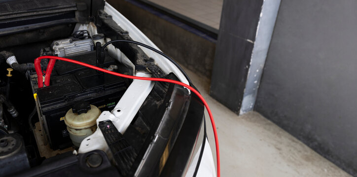 Car battery jump start with red and black jumper cables connected under open vehicle hood