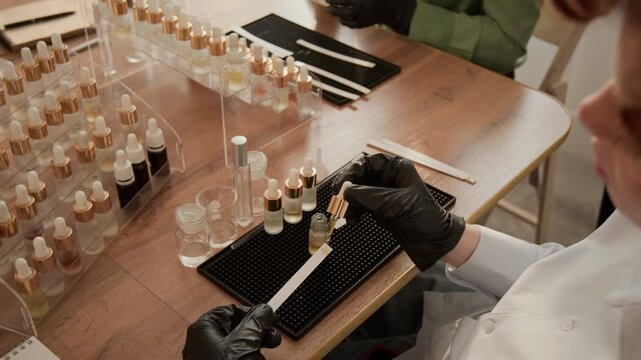 Caucasian woman wearing black gloves dripping essential oil from pipette onto paper tester strip during perfumery masterclass. Video suitable for promoting cosmetics brands or educational courses