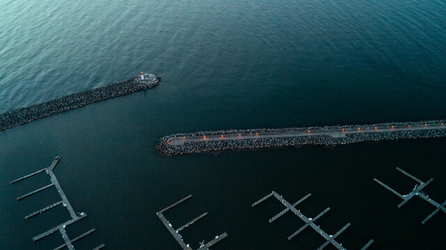A striking top-down drone photograph looking down at the stone breakwater walls and illuminated promenade pier protecting empty marina boat slips in the dark, calm waters of Bronte Harbour at dawn.