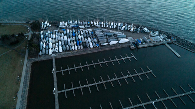 A high-angle drone photograph capturing tightly packed boats wrapped in winter shrink-wrap in a dry-dock storage yard next to rows of empty, quiet harbor docks on Lake Ontario at early morning dawn.