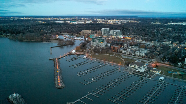 A beautiful high-angle drone photograph capturing the massive stone breakwater pier, empty winter boat slips, and the distant city skyline lights of Bronte Harbour at early morning dawn.