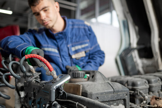 A professional mechanic in a blue work uniform is seen inspecting the intricate components of a truck engine under the hood. His expertise assures vehicle efficiency and dependable performance.