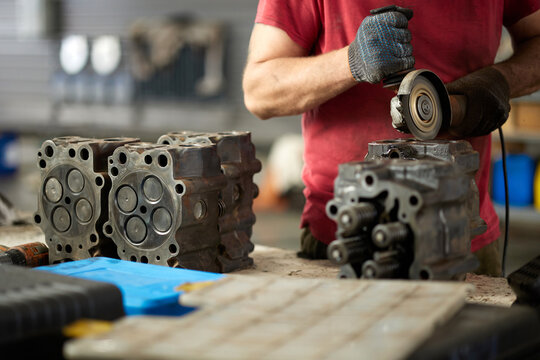 A skilled mechanic is seen performing maintenance on a truck, meticulously cleaning the cylinder head with a grinder. The industrial facility highlights a busy environment, showcasing expertise.