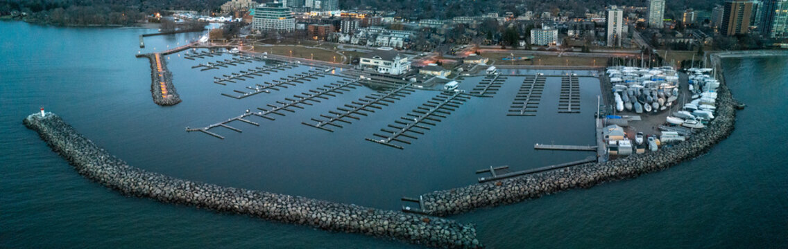 A stunning, wide panoramic drone photograph capturing the sweeping stone breakwater wall, rows of empty winter boat slips, and dry-docked yachts at Bronte Harbour on Lake Ontario at early dawn.
