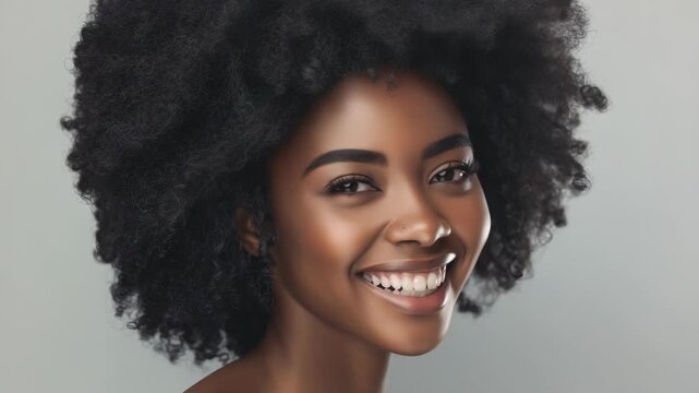 Close-up studio shot of a happy woman with a beaming smile, luminous skin, and an afro hairstyle. The minimalist background highlights her natural beauty and expresses joy.