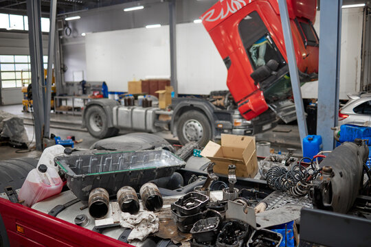 A detailed close-up of a disassembled engine in a machinery repair shop, with a raised cabin truck in the background. Tools and parts scattered around, showcasing the complexity of mechanical repairs.