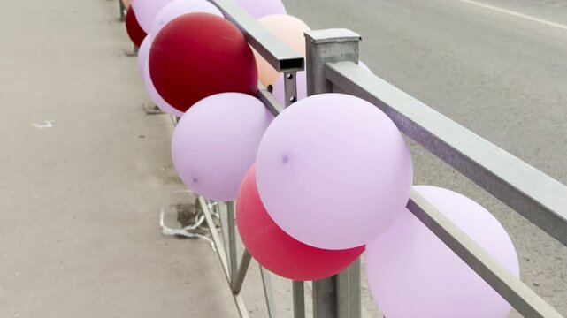 A row of colorful balloons tied to a roadside fence sways gently in the breeze. The passing traffic creates a constant, low rumble that vibrates through the air.