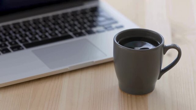 Minimalist black coffee in ceramic mug, laptop computer on wooden desk, modern home office workspace, professional remote work environment