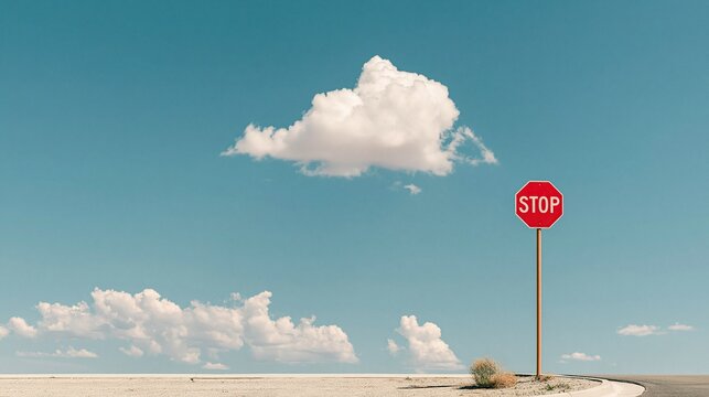 Red octagonal stop traffic sign standing alone beside empty asphalt road under bright blue sky with fluffy white clouds in open arid desert landscape
