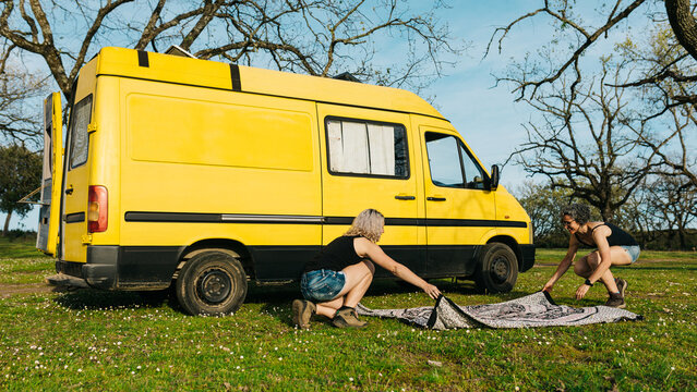 Women setting up campsite beside yellow camper van on holiday