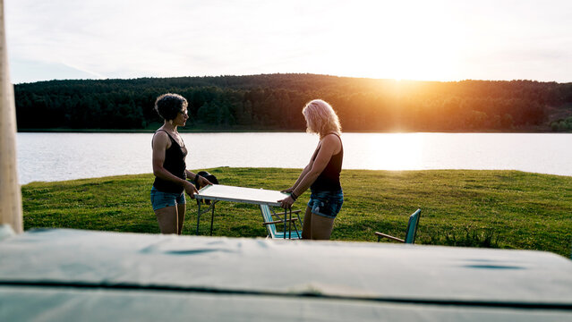 Women setting picnic table beside camper at sunset by lake