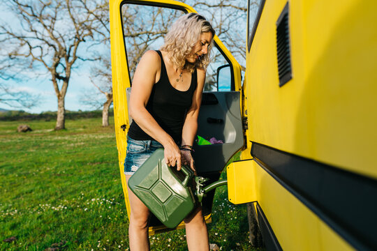 Woman refueling camper van with jerrycan on holiday trip