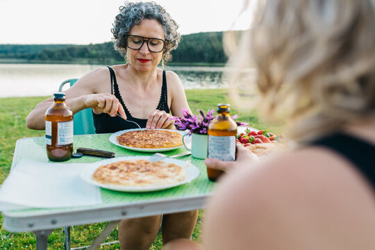 Women enjoying holiday picnic with Spanish tortilla by lake