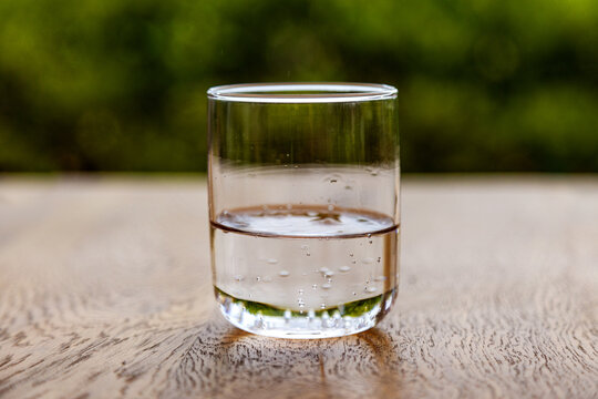 Glass of sparkling water on wooden table with green bokeh