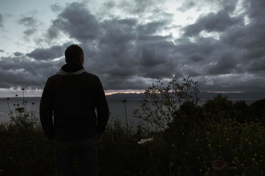 Silhouette of man near wildflowers at cloudy sunset coast