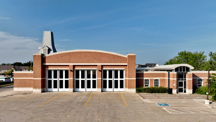 Aerial view of a generic brick fire station featuring large bay doors and arched entrance in a residential neighbourhood backdrop on a sunny summer day with a clear blue sky. © Barry Lavallee