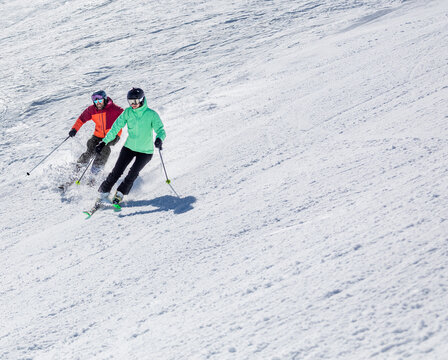 Couple skiing down snowy mountain in bright gear