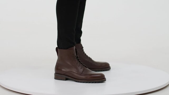 Man presenting elegant brown leather combat boots on a turntable isolated on a white background