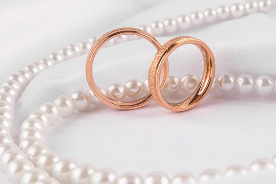 Elegant wedding rings and pearls on satin