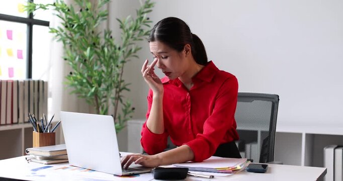 Young asian woman experiencing severe headache or migraine while working on laptop, suffering from stress, frustration, and exhaustion, touching temples due to intense pain and discomfort