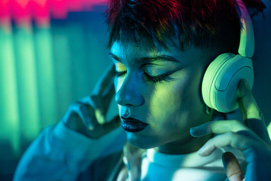 Young woman listening to music on headphones in neon light