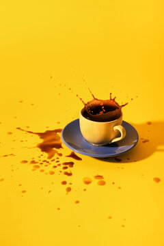 Black coffee splash in cup on saucer with yellow backdrop