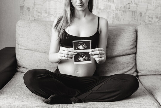 Pregnant woman holding ultrasound image at home