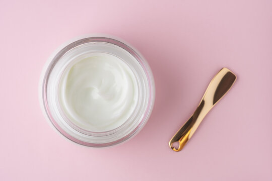 Cosmetic skincare cream jar with golden spatula on pink