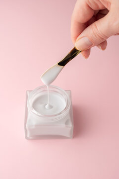 Cosmetic skincare cream jar with spatula on pink background