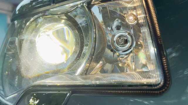 A powerful car headlight shines with an intense, bright glow. As the bulb illuminates the area, the running car engine generates a heavy, rhythmic idling sound.