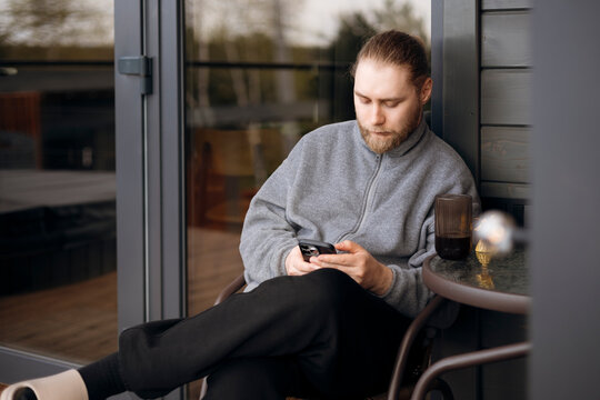 Man enjoying morning coffee outside while checking smartphone