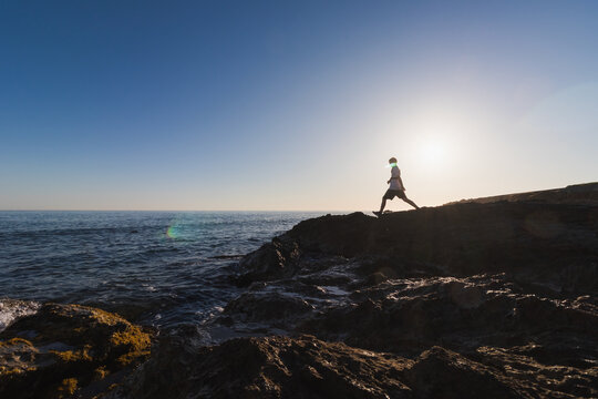 Silhouette of an 11 year old boy walking on rocky coast in Kato Gouves against the bright sun over the sea