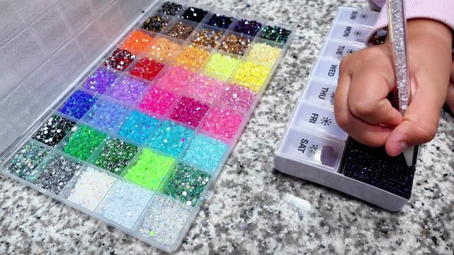 Horizontal 4K video of children's hands creating sparkling bedazzling crafts with gems and crystals, inspired by a popular DIY trend
