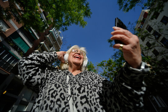 Senior woman on city street using smartphone with headphones