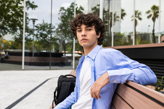 Curly haired man relaxing on bench in modern city plaza