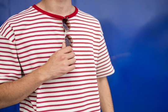 Man in striped t-shirt holding sunglasses on blue background
