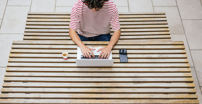 Curly haired man using laptop at outdoor table with coffee