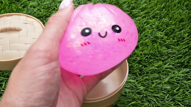 4K horizontal video of a hand squeezing a pink glittery dumpling squishy and lifting it out of a transparent plastic container. Cute sensory toy with sparkling texture, satisfying stress relief 