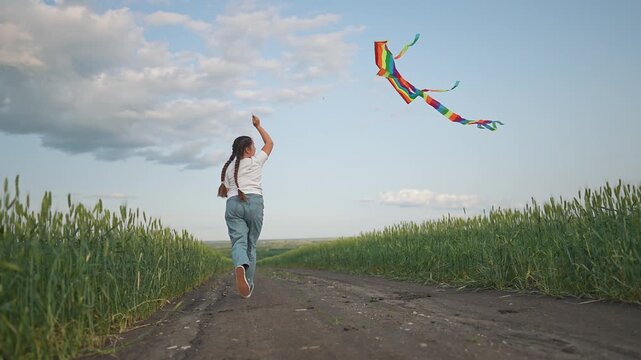 In the outdoor summer field, a girl runs with her kite in the wind. She plays under the open sky, chasing fun. The summer sun warms her face. The kite dances above the field, bringing joy to the girl.