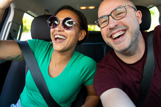 Happy diverse couple having fun taking a selfie while driving car on road trip