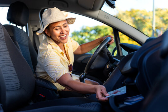 Happy woman reaching into glove compartment while driving car on summer holiday