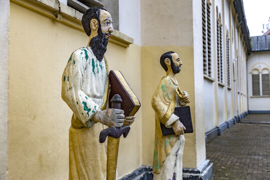 Douala, Cameroon - 28 April 2025: View of religious statues of saints holding books and a sword outside a historic church building with yellow walls and arched windows.