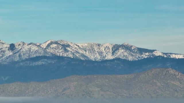 Aerial view of forested mountains with patches of winter snow under a cloudy sky in California