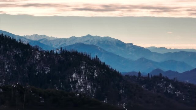 Aerial view of forested mountains with patches of winter snow under a cloudy sky in California