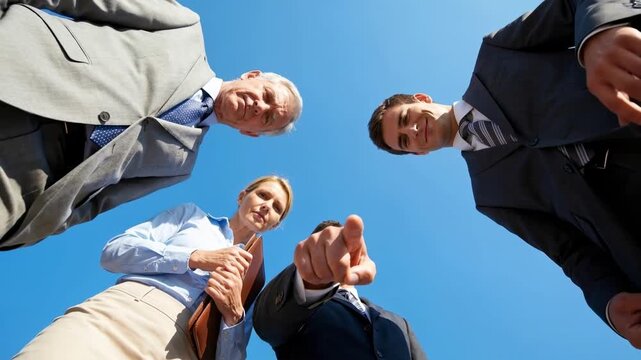 Low angle footage of a serious corporate business team looking down at the camera while a confident male manager points his finger directly at the viewer outdoors.