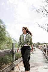 Fototapeta premium Young woman walking along beach boardwalk capturing authentic fashion and everyday coastal style