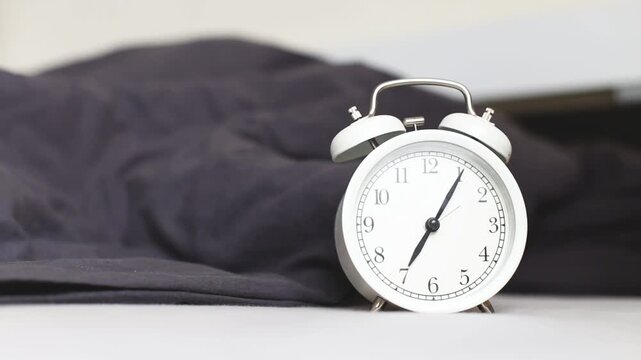 Sleeping person lying on the bed in bedroom and stopping alarm clock on bedside table at home. Wake up in morning of working day. Young child reaching for alarm clock to switch it off
