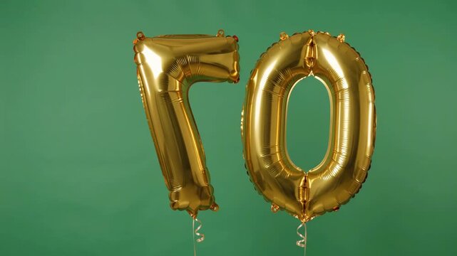 Golden foil balloons in the shape of number 70 slowly turning against a green chromakey background. Great element for editing a festive video for a 70th anniversary.