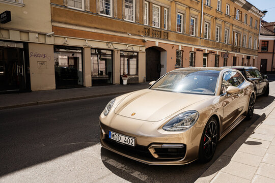 Golden Porsche Panamera parked on a sunny street in Vilnius, Lithuania reflecting historic yellow facades and urban elegance